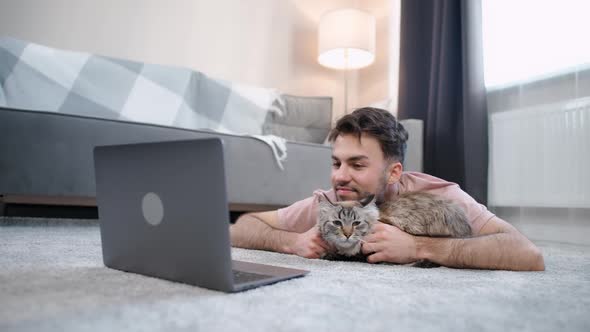 Young Man with a Cat Lies on the Floor in the Living Room and Works at a Laptop Selfisolation