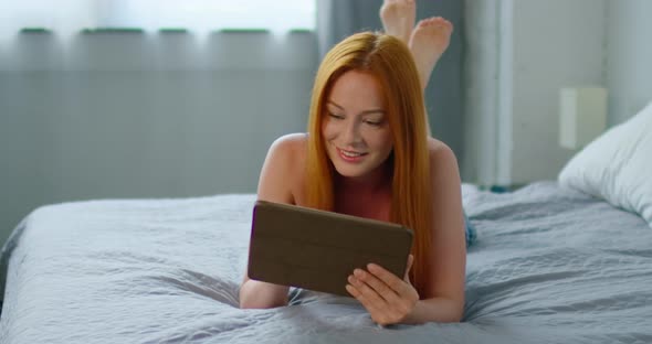 Pretty Woman Is Relaxing in Bed, Using Tablet Computer