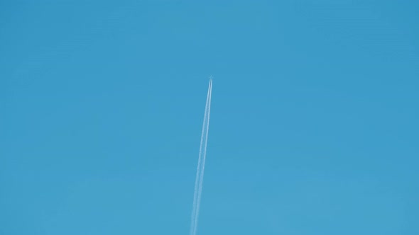 Distant Passenger Jet Plane Flying on High Altitude on Clear Blue Sky Leaving White Smoke Trace of