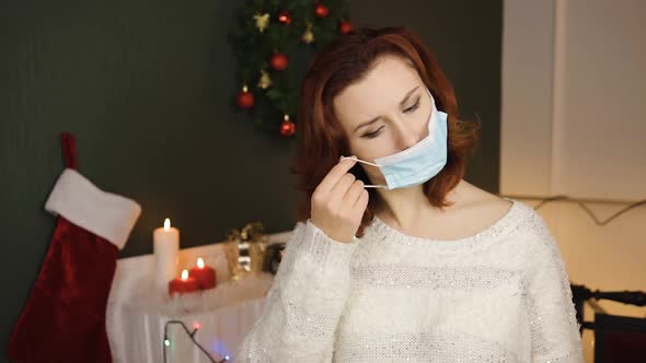 Cute Young Woman Puts on Medical Mask Feeling Down with Gift Box in Hands
