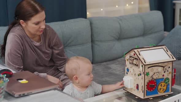 Mother and Her Baby Boy Playing with Wooden Busy House Montessori Educational Toy at Home