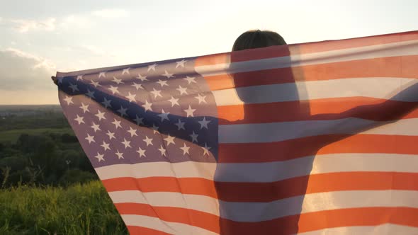 Young woman with USA national flag walking outdoors at sunset. Positive girl celebrating 