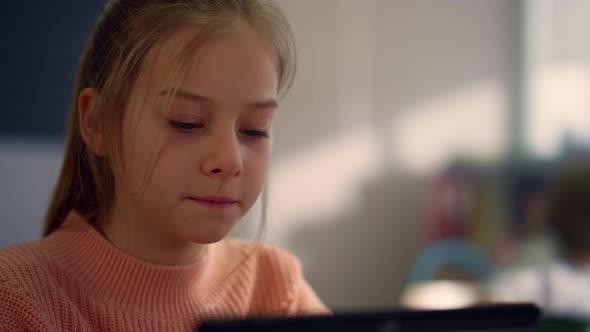 Diligent Student Reading Book on Digital Tablet at Lesson in Classroom