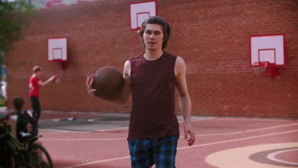 Young Man Running on the Basketball Playground and Hitting the Ball - Looking in the Camera