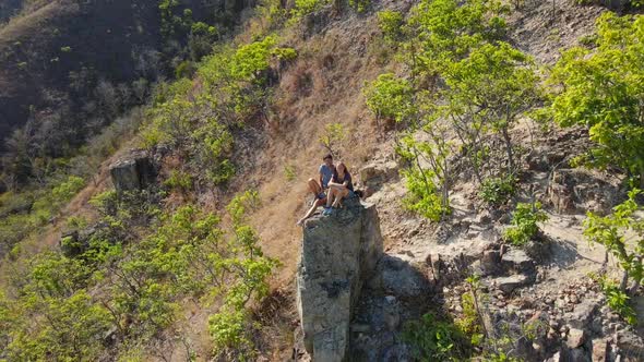 Aerial Shot of a Young Man and Woman Sitting on a Rock in Mountains. Hiking Concept