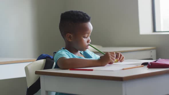 Video of african american boy sitting at desk during lesson in classroom