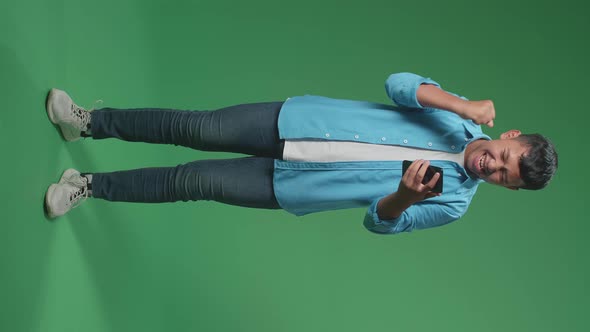 Young Asian Boy Celebrating With Mobile Phone While Standing On Green Screen In The Studio