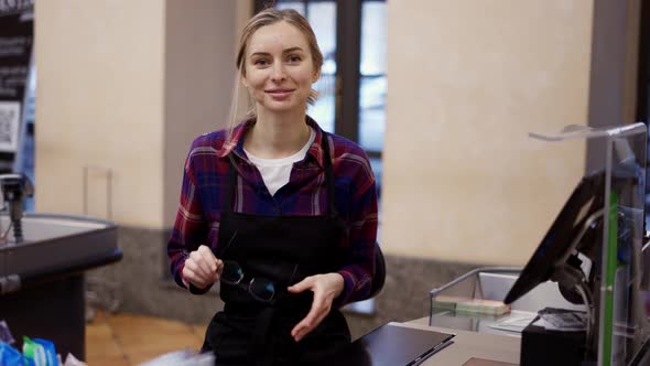 Woman Putting on Eyeglasses Working at the Checkout in a Supermarket