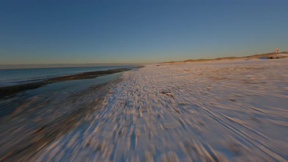 Aerial Drone FPV Hovering Above Sea Shore Filled with Snowy Patches By Beach