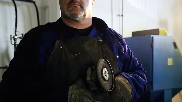 Welder holding electric saw in workshop