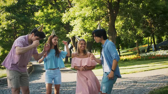 Happy Young Friends in Party Hats are Laughing and Dancing in Green Landscaped Park