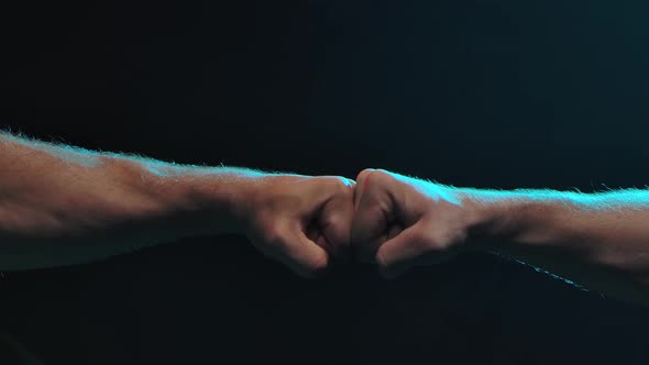 Conflict Concept. The Clash of Two Fists of Male Athletes on a Black Background. Slow Motion