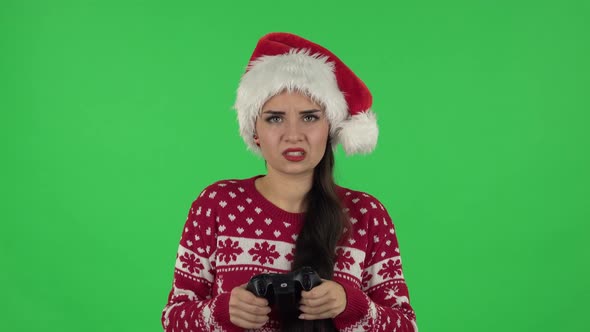 Portrait of Sweety Girl in Santa Claus Hat Is Playing a Video Game Using a Wireless Controller and