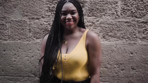 Plump black woman laughing against rough stone wall in town