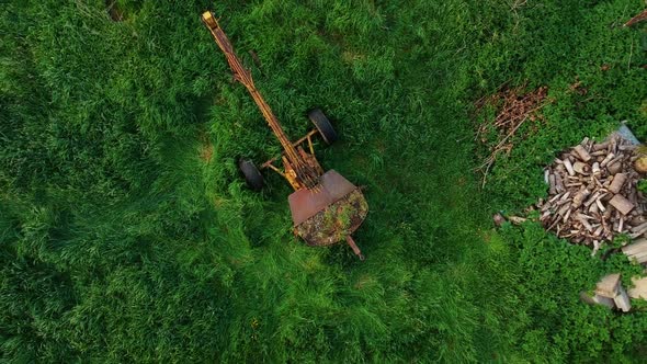 Rising overhead shot, old excavator and junk in overgrown green field
