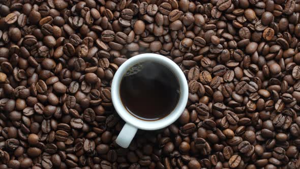 White cup of hot coffee and rotating background of fresh roasted coffee beans