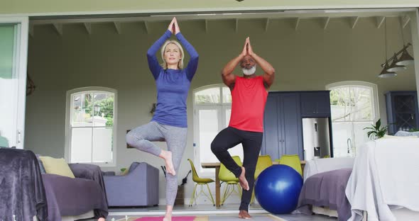 Mixed race senior couple practicing yoga together at home