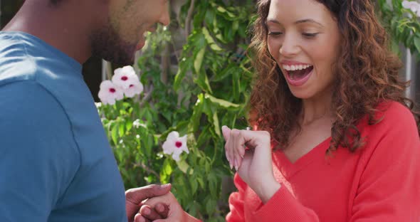 Happy biracial woman looking at hand with ring after proposal