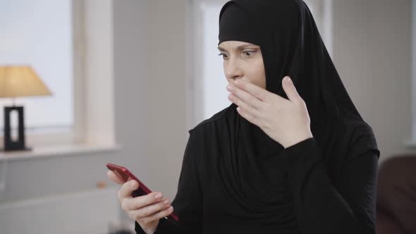 Young Muslim Woman in Traditional Hijab Looking at Smartphone Screen Amd Making Shocked Facial