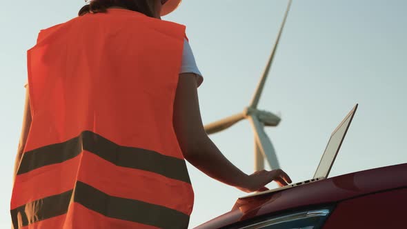 An Windmill Engineer Supervises the Work of the Wind Turbines on the Laptop Standing Near the Car