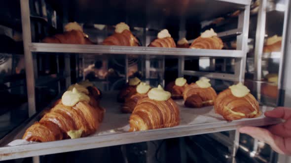 Baker Puts Baking Sheet of French Croissants with Almond Paste in the Oven to Bake