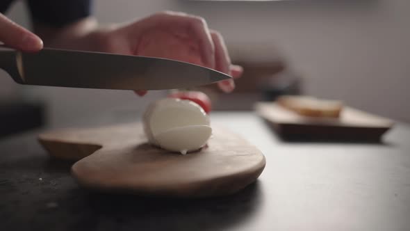 Slow Motion Man Slicing Mozzarella Ball on Olive Wood Board