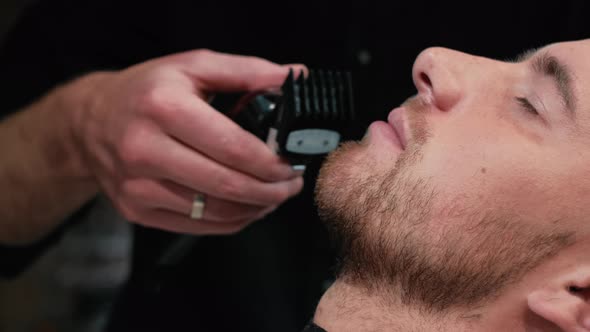 Barber Shaves the Client's Beard on a Chair. Beard Haircut. Barber To Shave a Beard with an Electric