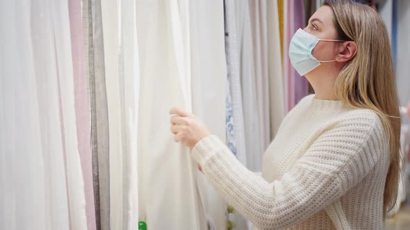 a Woman in a Protective Mask Sorting Through Various Thin Curtains Choosing Textiles for the Home