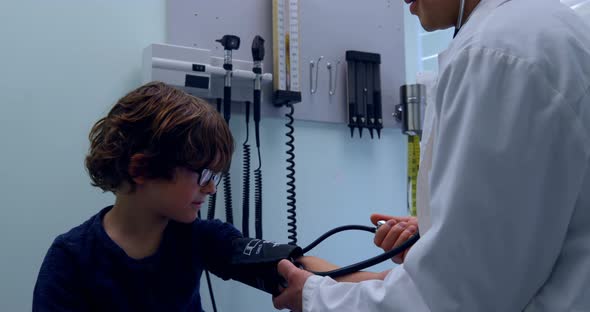 Side view of young asian male doctor checking blood pressure of caucasian boy patient in clinic 4k