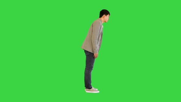 Young Asian Man in Casual Clothes Makes a Bow on a Green Screen Chroma Key
