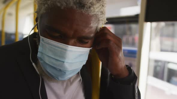 African american senior man in face mask wearing earphones while standing in the bus