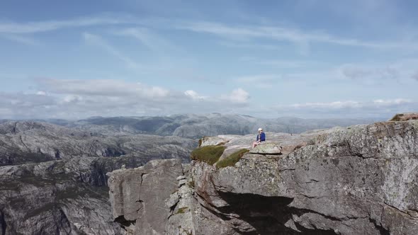 Aerial Shot of a Female Hiker Wearing Blue Jacket Sitting at the Edge of a Cliff