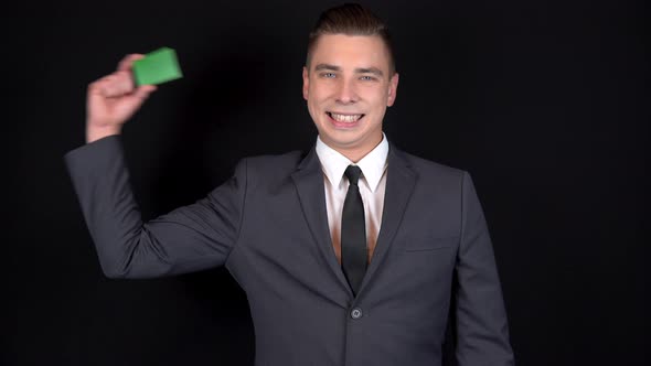 A Young Businessman Presents a Green Bank Card. Chromakey Green Card. Man in a Black Suit