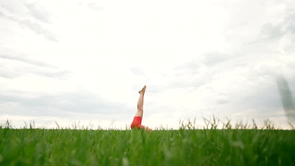Strong Woman in Orange Wear Doing Yoga Sarvangasana  Shoulder Stand Inverted Asana in Green Field