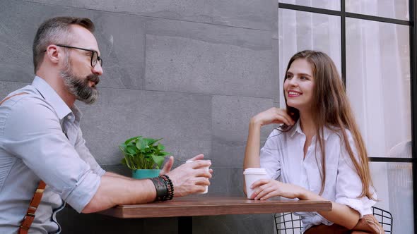 confident man and woman enjoying coffee and smiling while sitting on cafe terrace.