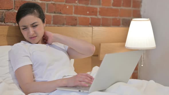 Young Indian Woman with Neck Pain working on Laptop in Bed