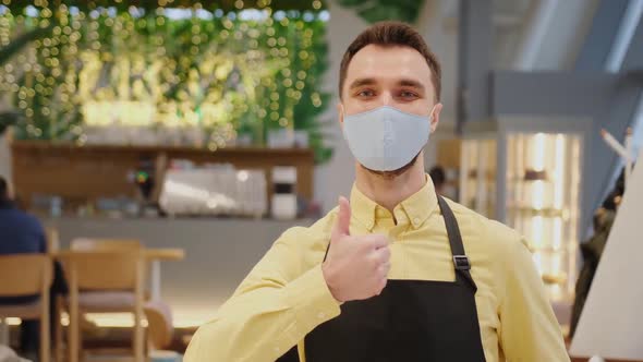 Male Waiter Cafe Owner Wearing Mask and Gloves Stands and Shows Thumb