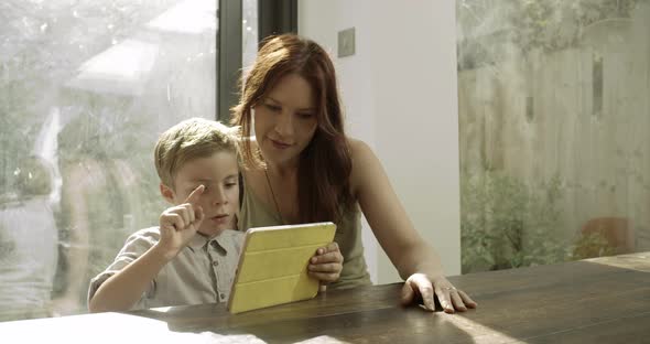 Mother and son using digital tablet in domestic room 