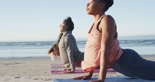 Group of diverse female friends practicing yoga, stretching at the beach