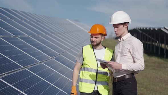 Businessman and Worker Are at the Solar Power Station Discussing the Project