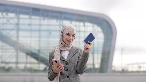 Muslim Lady in Hijab Standing Outside in Front of Airport Terminal and Holding Phone and Passport