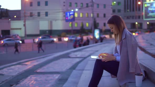 The Girl Works in the Tablet, in the Evening in the City Center.