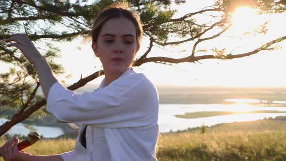 Swords Training Young Pretty Woman in White Shirt Waving with a Sword Outdoors at Early Evening on