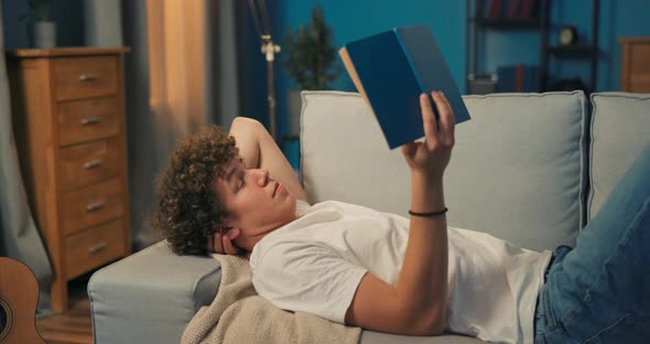 A Young Boy with Dark Curly Hair is Lying on a Couch in the Living alt