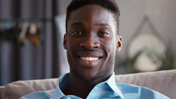 Smiling young adult man looking at camera on the couch, close-up