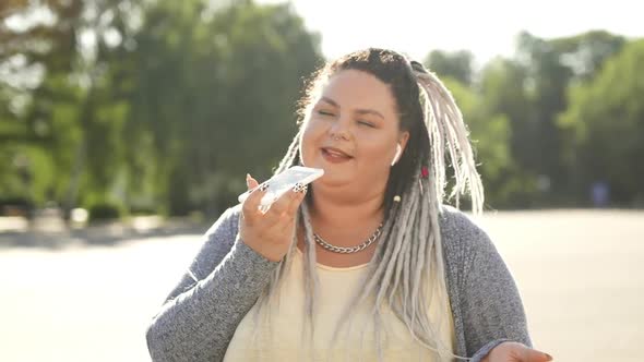 Female Holdig Mic To Fix Her Ideas. Happy Fat Woman Recording Audio Message Standing on Street at