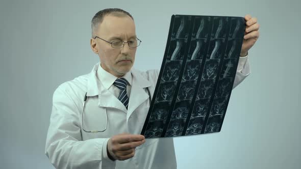 Serious Physician Checking Injured Spine Scanning Image, Looking at Camera