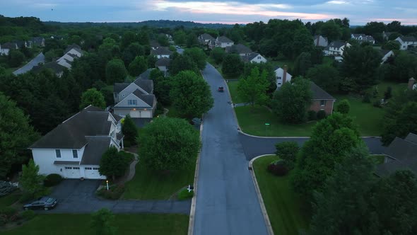 Aerial view of a quiet street in affluent neighborhood at dawn/dusk. Sunrise or sunset is visible be