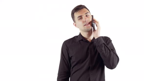 Laughing Young Man in Black Shirt Talking By Mobile Phone Over White Background