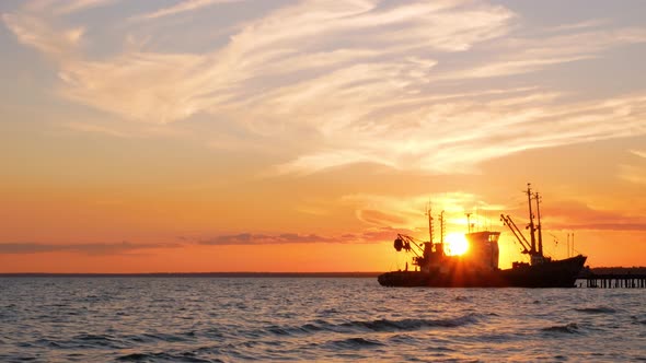 Beautiful orange sunset on sea water. Transport ship on the dock in the evening on seacoast.